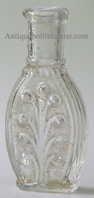 An early colorless beaded plume with opposite side featuring a beaded oval space, likely used for a label. A pontil mark is on the base. Height, 2 - 7/8 in. Width, 1 - 3/8 in. --- AntiqueBottleHunter.com