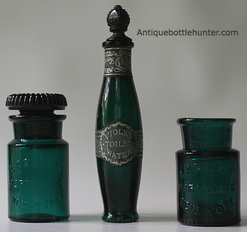 Three LAZELL'S bottles in various shades of teal. Two salts bottles embossed the same, flanking a toilet water. The left one has more of a shoulder to it and an embossed (script monogram) ground stopper. The middle bottle is embossed on the opposite side: LAZELL'S / NEW YORK /PERFUMES. It has two black and silver labels. One states: Violet Toilet Water... and the other mentions: Lazell, Dalley & Co. We're not sure if the fancy stopper is original, but it looks great. The far right variant has a crude lip and the shoulder is at a sharper angle. --- AntiqueBottleHunter.com